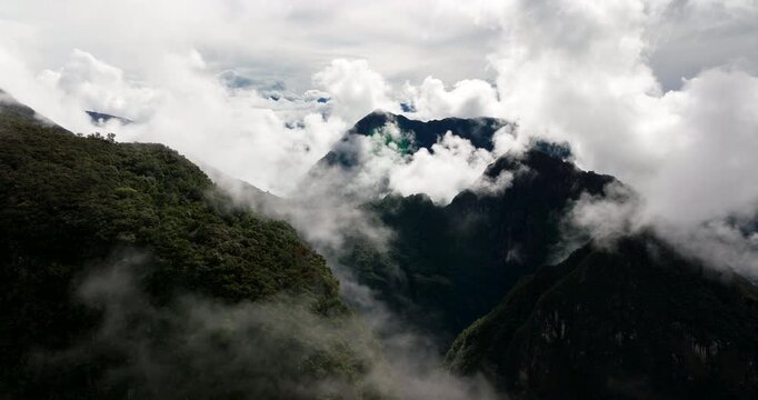 Aerial drone view flying through dense fog and clouds, revealing lush green mountain peaks in Andes near Machu Picchu, Peru