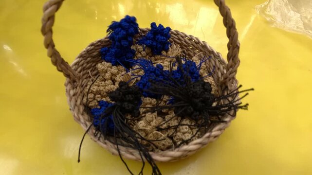 Small woven basket filled with Moroccan aqad knots, handmade textile fasteners used in traditional caftans and djellabas, showcasing artisanal craftsmanship, precision and cultural heritage.