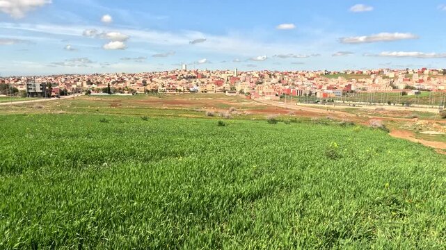 Rural landscape of Tahla in northern Morocco, featuring green farmland, rolling hills and expanding town buildings, reflecting agricultural life and a calm countryside atmosphere.