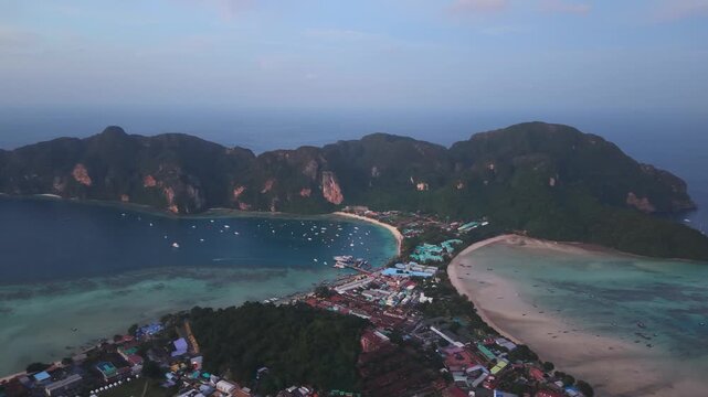 Drone sunset view of Koh Phi Phi isthmus twin bays, turquoise water and anchored boats, local residence nearby aerial view.