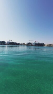 Ayla Marina Aqaba with clear turquoise water waves and Luxury yacht docked in vertical view, coastal city.