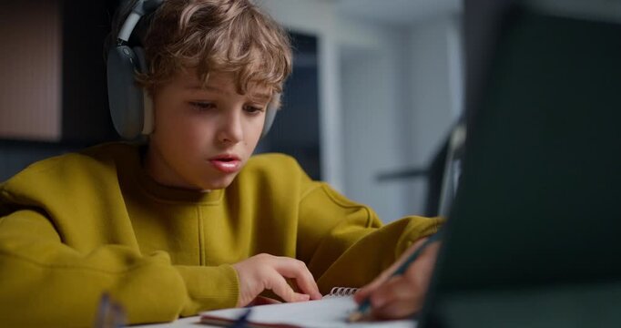 Teenager With Tablet And Notebook Focused. Young Boy Wearing Headphones Working On His Assignments