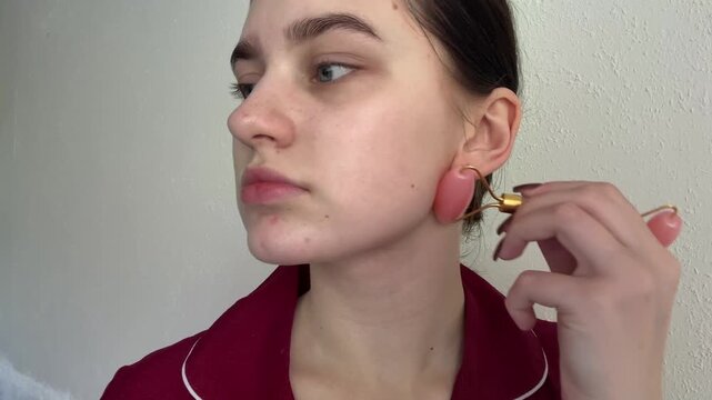 Woman performing soothing face roller massage, applying gentle pressure to her cheekbone and jawline, enhancing youthful skin texture, demonstrating a daily beauty routine.