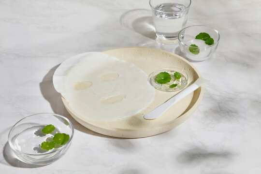 Flat lay composition with facial mask, centella leaves and bathroom tools on clean surface. Spacious layout with wide copy space for cosmetic branding, product mockup and advertising design.