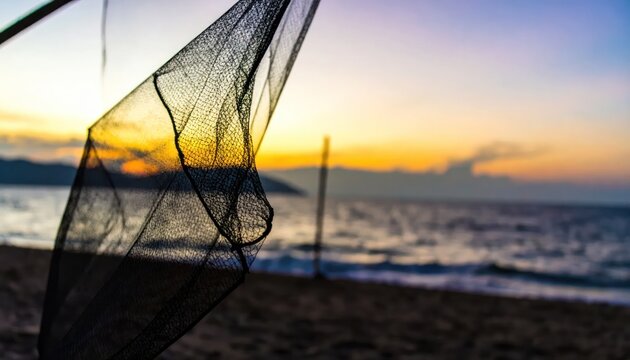 Detailed black fishing net silhouette against a vibrant golden hour sky and serene ocean landscape at a peaceful tropical beach during sunrise or sunset
