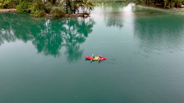 Two adventurers glide across the serene waters of Koh Kood Island, surrounded by lush greenery. This idyllic setting showcases the natural beauty of Thailand. a couple in a kayak in the ocean