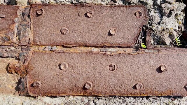 Macro top down view of heavily corroded riveted steel girder of an old pier with layered rust and pioneer succulents. Industrial heritage in summer
