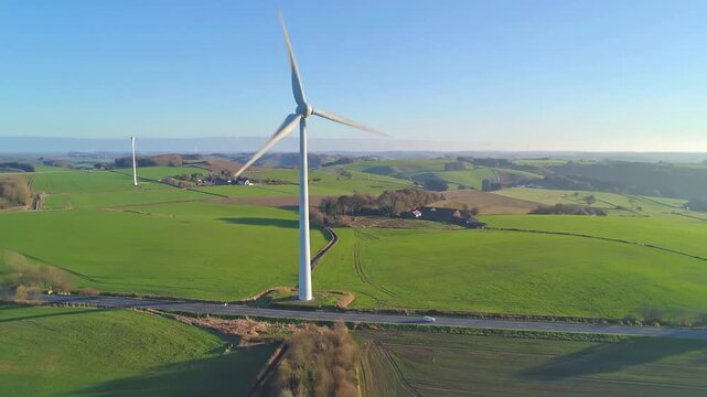 A tall wind turbine stands in a green field under a clear sky