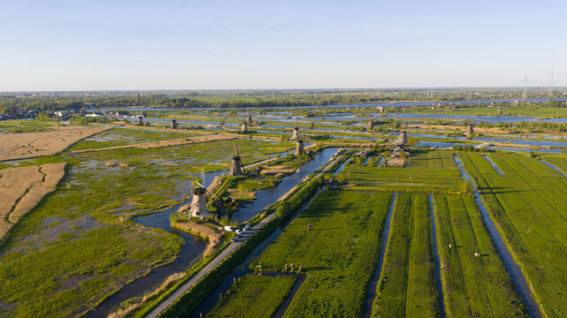 Aerial view of historic windmills standing along narrow canals amidst lush green fields and polder landscapes under a clear blue sky Kinderdijk, South Holland, Netherlands.