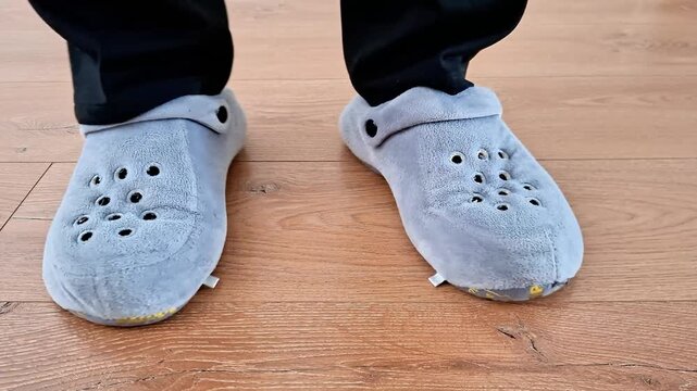 Close up of person wearing soft gray slippers standing on wooden floor, gently shifting feet. Cozy indoor scene highlighting comfort, home relaxation, and casual lifestyle vibes