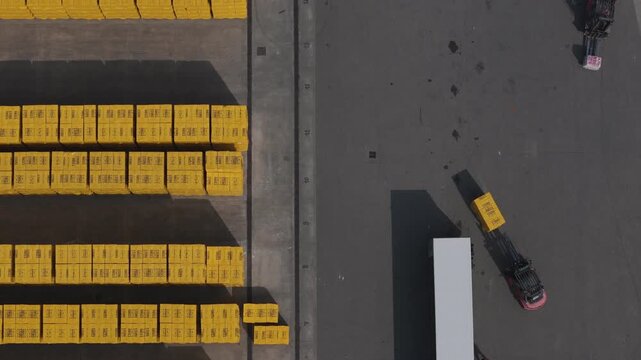 Forklift operating in logistics yard in Po Valley Emilia Romagna Italy handling stacked construction blocks near truck trailer within industrial storage area, drone top down shot