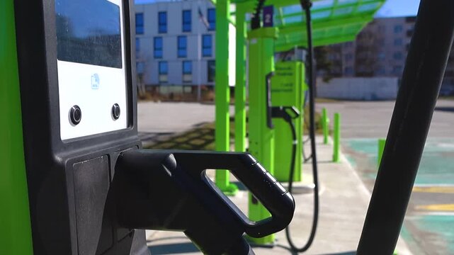 Row of empty electric vehicle charging stations in an urban parking lot on a sunny day with modern buildings in the background, promoting green energy and sustainable transportation