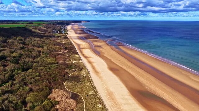 Drone shot of long tidal beach with dunes, sea, and distant cliffs. Normandy, France