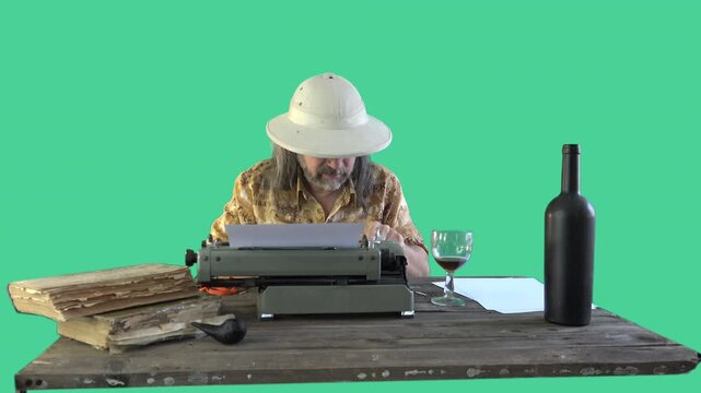 Middle aged man in safari hat using old typewriter at wooden desk with chroma key background and vintage travel atmosphere