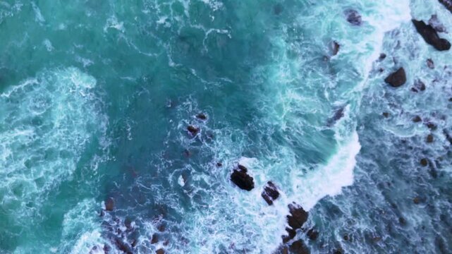 Drone shot of turquoise ocean flowing around scattered rocks with soft wave motion.