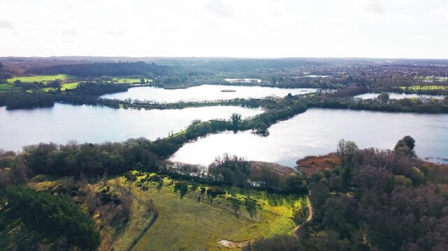 Drone view over multiple connected lakes in Somerset wetlands with tree-lined banks and open countryside creating layered water patterns
