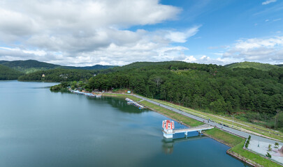Naklejka premium A scenic view of Tuyen Lam Lake in Da Lat, Vietnam, with boats docked along the shore and lush green hills in the background under a cloudy sky.