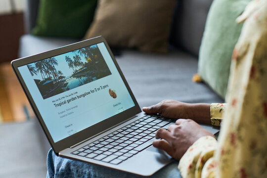 Young adult woman browsing resort booking on laptop while preparing for trip, comparing travel accommodation options. Useful for vacation planning, tourism marketing, online booking