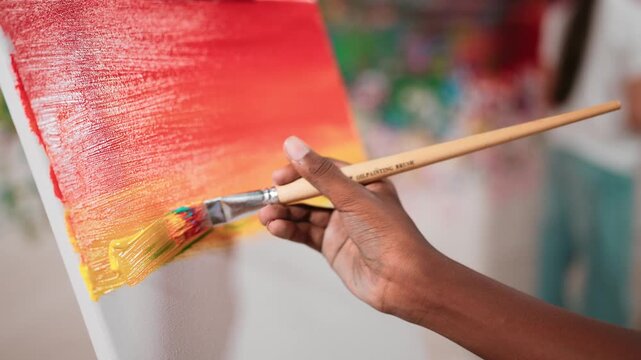 Closeup of african boy hand paint canvas with warm tone color while caucasian girl in casual outfit drawing cool tone colors behind at colorful stained wall. Creative activity concept. Edification