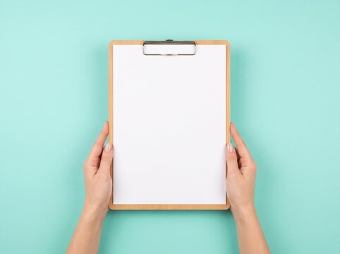 A pair of hands holding a blank clipboard with a white sheet of paper against a teal background.