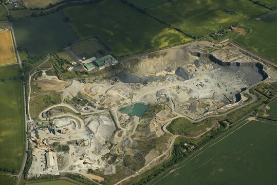 Aerial view of Roadstone Kilmacow quarry with industrial machinery, gravel piles, and a small pond surrounded by green fields in Kilmacow, County Kilkenny, Ireland.