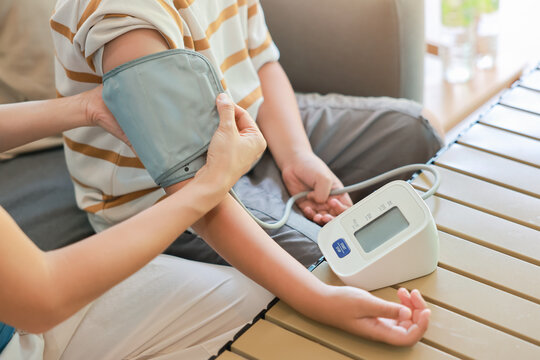 Close up unrecognizable mother hands applying blood pressure cuff on her son arm for measuring with automatic digital monitor at home. Family pediatric healthcare and daily wellness medical