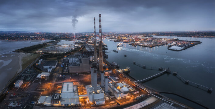 Aerial view of Poolbeg Power Station with its iconic red and white chimneys illuminated at dusk overlooking Dublin Port and the city skyline in Dublin 4, County Dublin, Ireland.