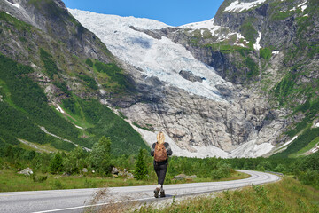 Fototapeta premium Back, woman and hiking on road with backpack for travel, adventure and backpacking holiday. Mountain, female person and walking for trekking journey, glacier scenery and explore nature on vacation