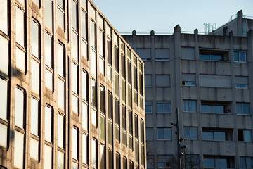 Modern office building with glass windows next to a concrete apartment block in Lille, France. The sun reflects off the glass facade during late afternoon. © dsbedarieva