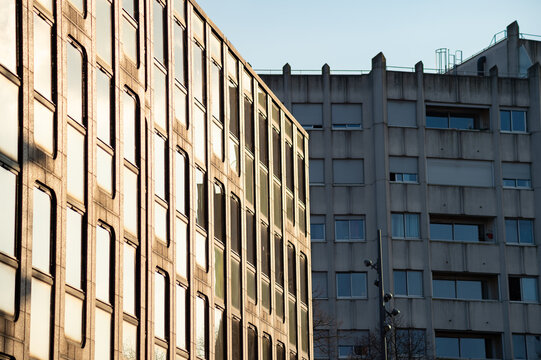 Modern office building with glass windows next to a concrete apartment block in Lille, France. The sun reflects off the glass facade during late afternoon.