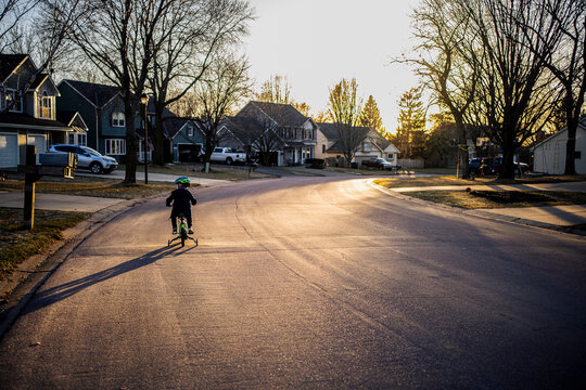 Young Boy Riding Bicycle Down Backlit Suburban Neighborhood Street