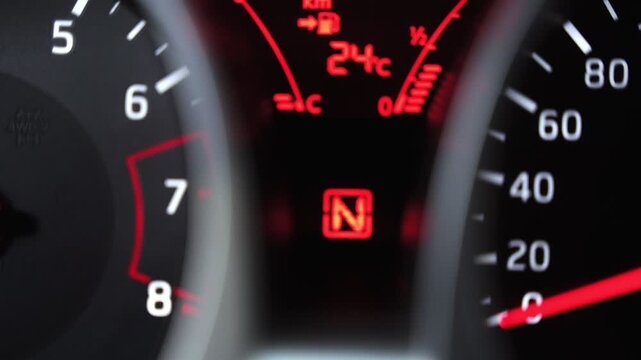 Extreme close-up of a digital vehicle dashboard shifting gears from Reverse to Low. Red illuminated indicators show the gear position, temperature, and fuel levels in a modern car.
