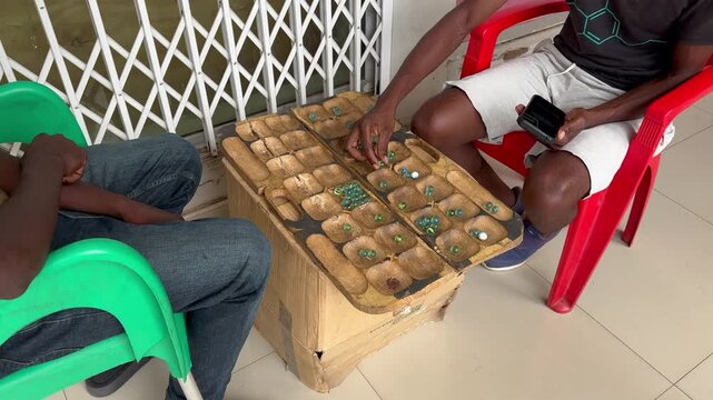 Two men playing bawo - traditional Malawian strategy board game belonging to the Mancala family.