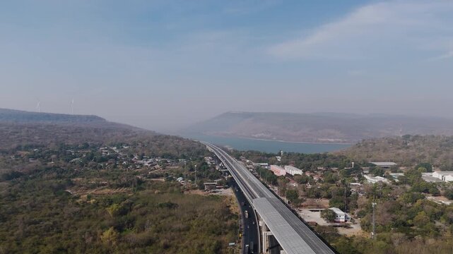 Aerial view of highway running along river and green hills. Transportation, infrastructure, travel and logistics concept