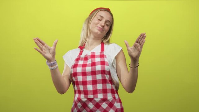 Woman cook in red checked apron wearing red headband and white tee with hands open and smiling face in studio; joyful cooking.