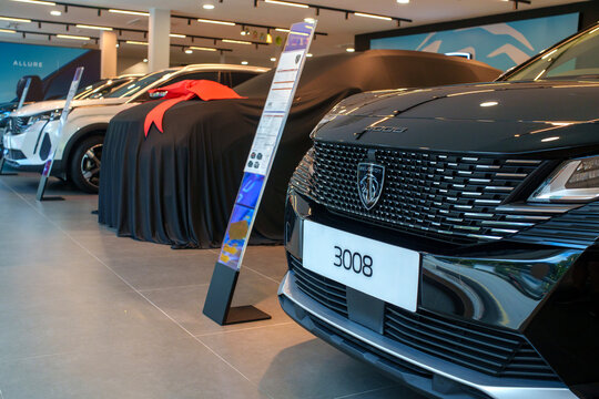Penang, Malaysia - Apr 07, 2026: A black Peugeot 3008 SUV on display in a modern dealership next to a new vehicle covered in a black cloth with a large red gift ribbon, ready for a customer delivery.
