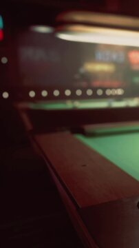 People play a game of pool at a bar. The scene shows a green pool table with a cue ball and players focused on their shots. Soft lights create an inviting atmosphere.