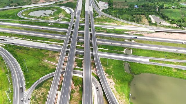 Aerial view of modern highway interchange with multilayer roads and curved ramps surrounded by green farmland, showcasing transportation infrastructure, urban development, and road network planning.