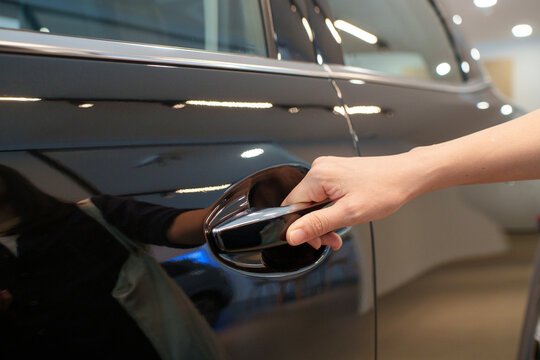 A close-up view of a hand reaching for and pulling the chrome door handle of a modern SUV car.