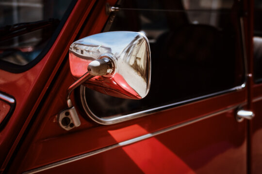 Chrome side mirror on a red vintage car parked on a sunny street
