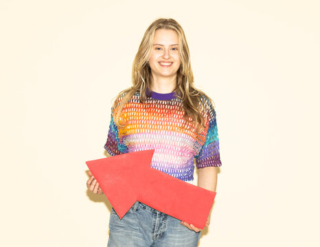 Smiling model in sweater holding red arrow indoors for strategy