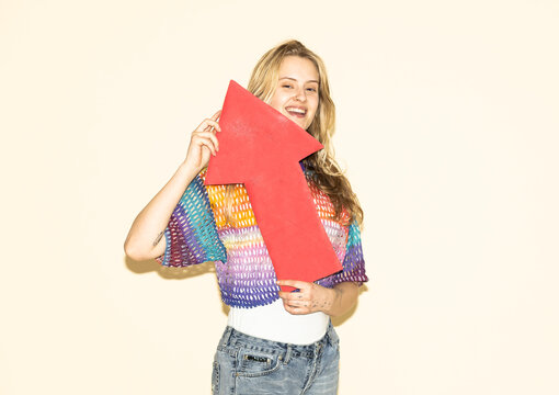 Smiling woman holding a red paper arrow pointing upwards