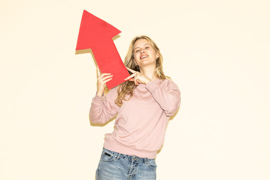 Smiling woman pointing red paper arrow upwards indoors