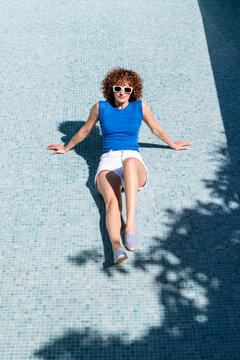 Smiling female tourist in sunglasses sitting in empty pool