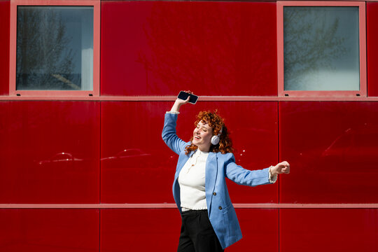 Businesswoman dancing outdoors with headphones and smartphone