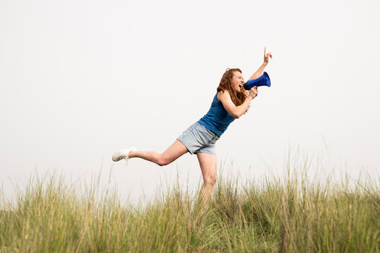 Woman shouting into a megaphone and jumping in a field