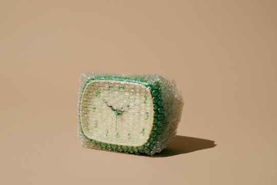 Vintage alarm clock wrapped in bubble wrap on beige background