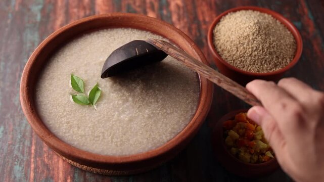 Millet porridge in a mud plate on a wooden table. Millet porridge with lentils healthy breakfast or dinner. Diabetes friendly meal. Kanji fox tail millet in Kerala India.
