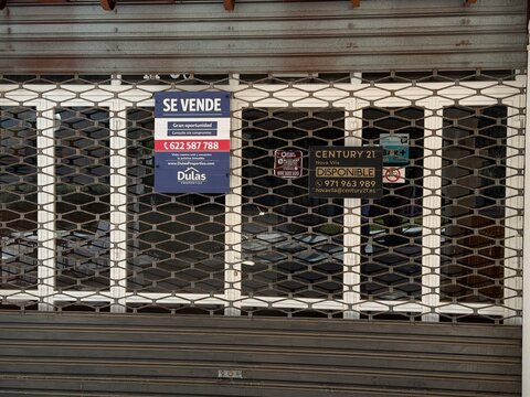 Palma, spain, may 2, 2026, closed storefront with se vende and disponible signs behind a metal security gate, reflecting economic challenges