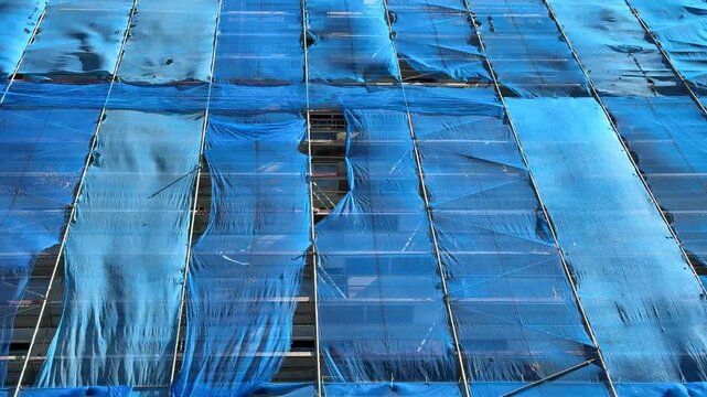 Blue construction safety net on building scaffolding moving in wind. Urban renovation process and dynamic fabric motion on facade structure concept.